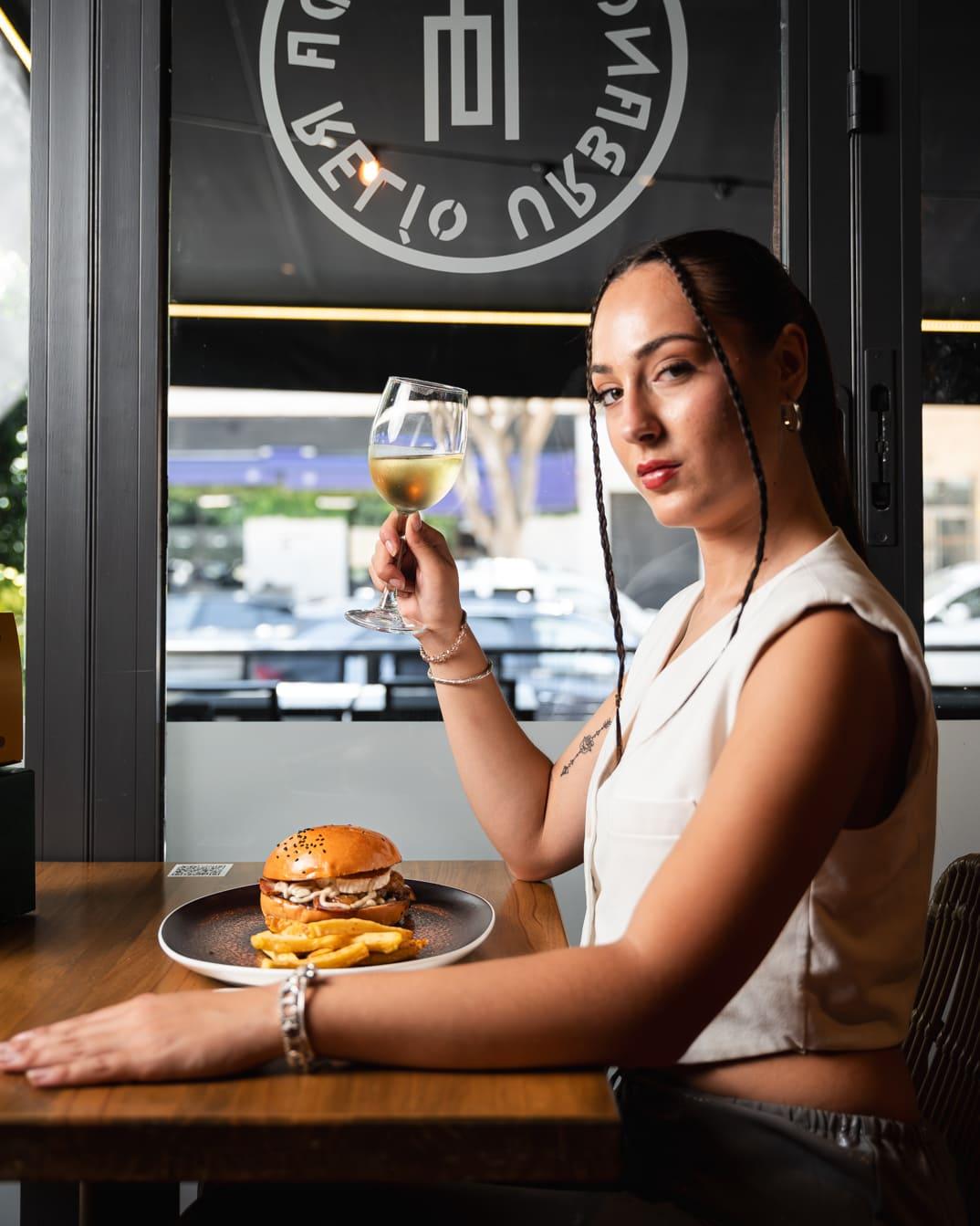 Mujer por probar una hamburguesa con una copa de cerveza en la mano